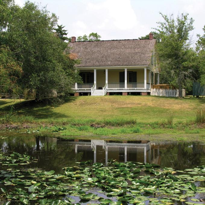 Lily pads float in a pond in front of a country house in Vermilionville