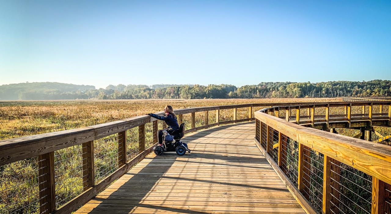 Visitante apreciando o espetacular pôr do sol no acessível Neabsco Creek Boardwalk, no Condado de Prince William, Virgínia